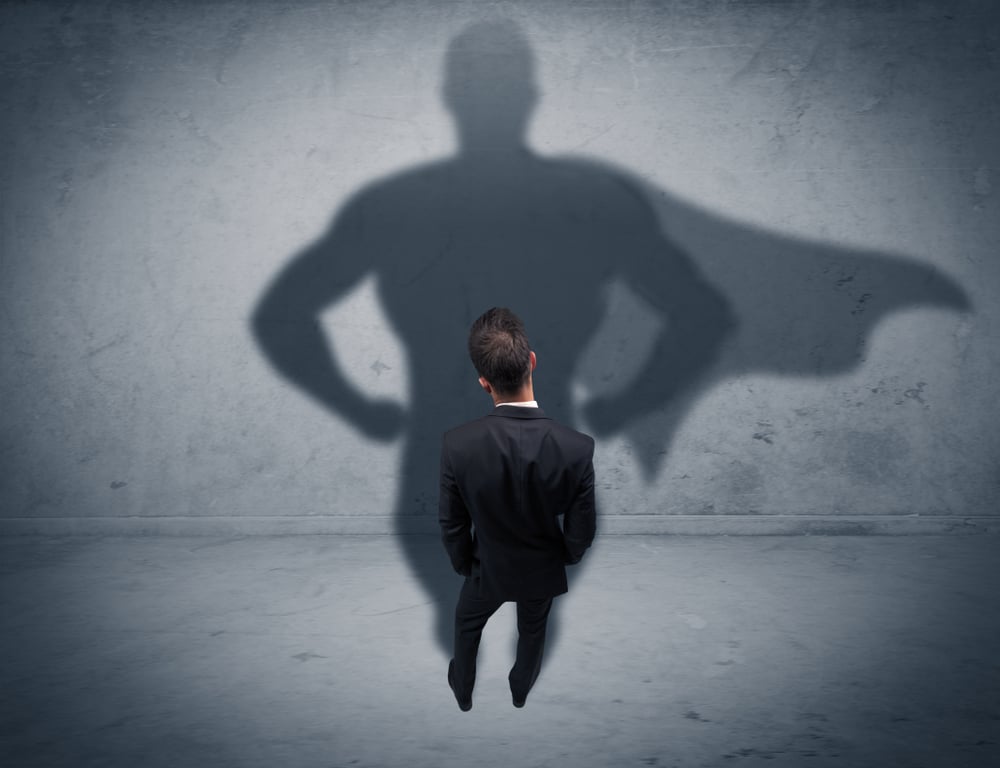 A confident young elegant salesman with briefcase facing a wall, looking at his superman shadow concept